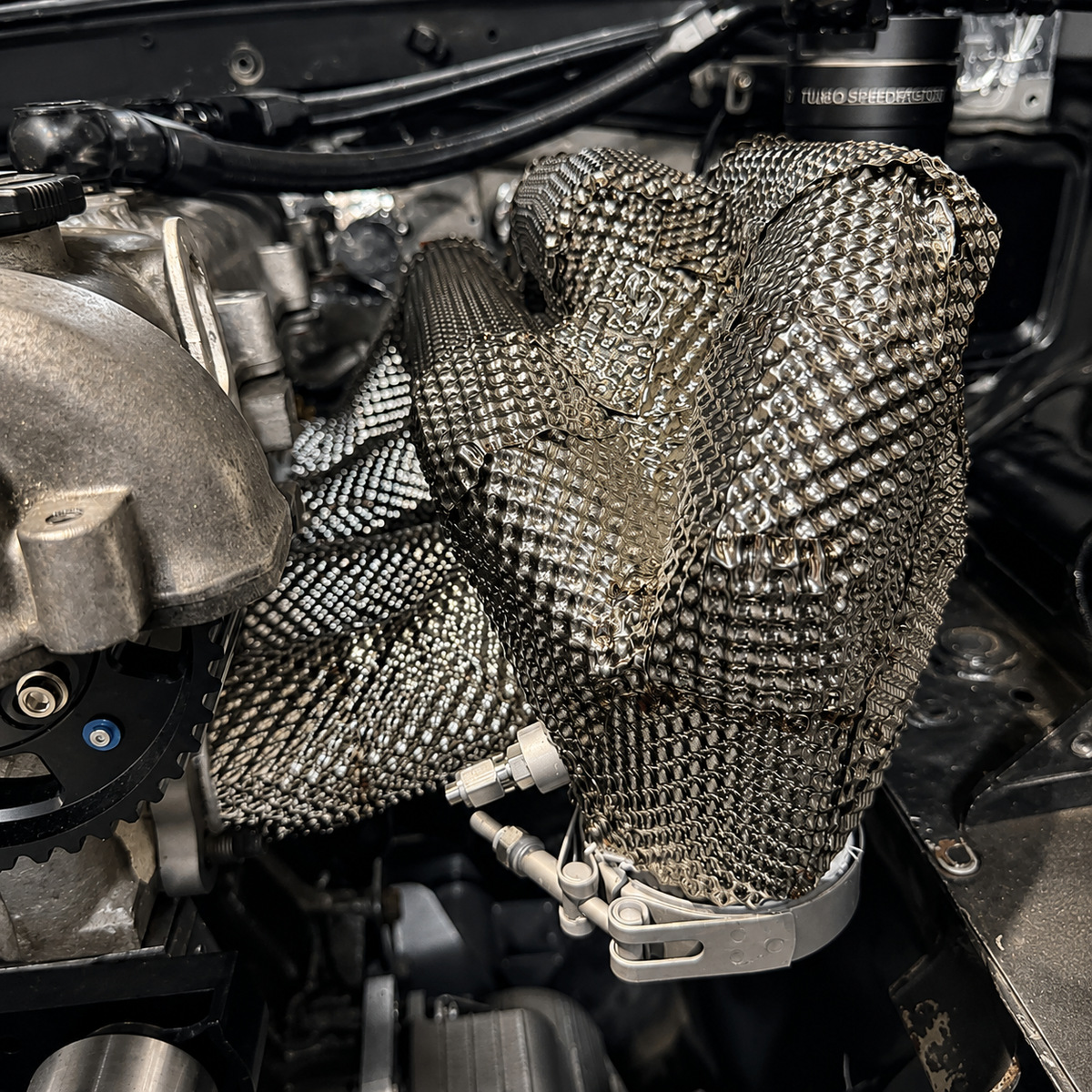 Custom fabricated stainless exhaust heat shield installed around pipework in an mx-5 engine bay